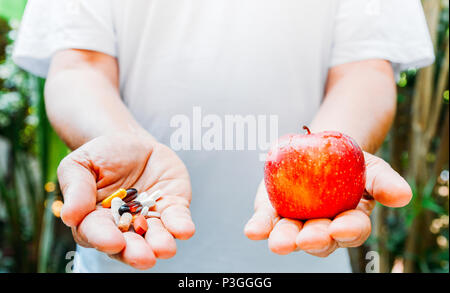 Person hält einen roten Apfel in der einen Hand und eine Handvoll Pillen in den anderen Stockfoto