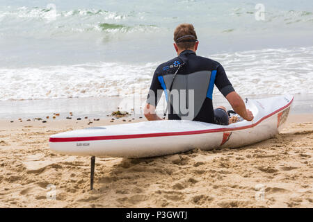 Man sitzt in einem Surf Ski surfski, der am Ufer des Meeres in Branksome Chine, Poole, Dorset, England Großbritannien im Juni Stockfoto