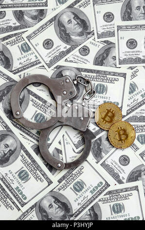 Polizei Handschellen und Bitcoins liegen auf eine große Anzahl von Dollarnoten. Das Konzept der Probleme mit dem Gesetz während der Illegalen cryptocurrency Bergbau- und Stockfoto