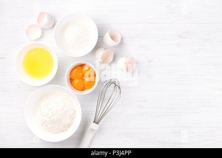 Zutaten zum Backen Biskuit. Eier, Mehl, Zucker und Schneebesen. Ansicht von oben Stockfoto