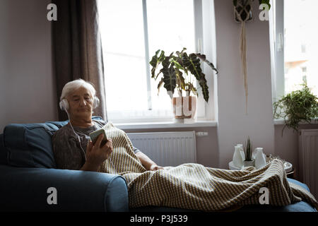 Ältere Frau Hören von Musik über Kopfhörer, während mit Handy Stockfoto