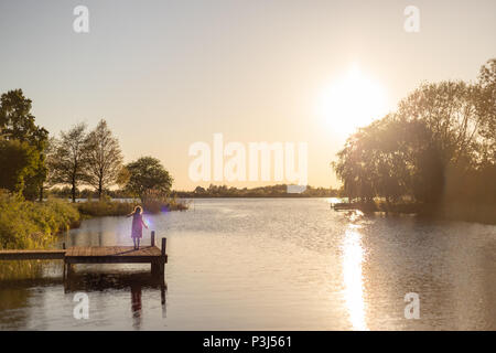 Ein 7 Jahre altes Mädchen ist spielen und Tanzen auf einem Holzsteg an einem See in den Sonnenuntergang Stockfoto