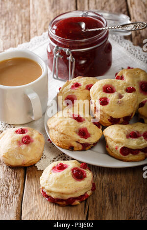 Hausgemachte Wandleuchten mit roten Johannisbeeren sind mit Englischer Tee mit Milch und Marmelade in der Nähe serviert - auf den Tisch. Vertikale Stockfoto