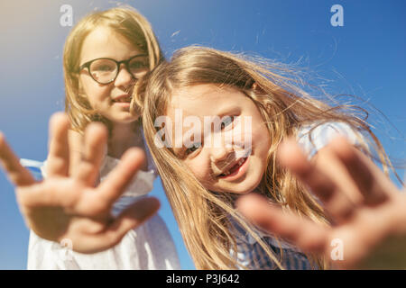 Zwei fröhliche Mädchen auf der Suche an Kamera und dehnen Ihre Palmen. Aufrichtiger Emotion. Mädchen ohne vorderen Zähne. Stockfoto