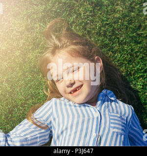 Kleines Mädchen mit Kamera, lächelnd und liegen auf dem Rasen. Sommer Freizeitaktivitäten. Mädchen ohne vorderen Zähne. Stockfoto