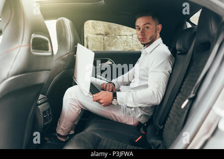 Selbstbewussten jungen Geschäftsmanns, der auf seinem Laptop im Auto sitzen Stockfoto