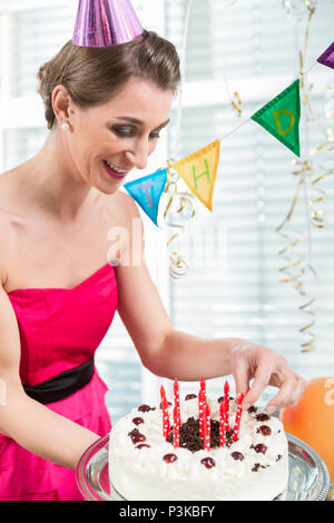 Porträt einer schönen Frau lächelnd und mit roten Kerzen auf Kuchen Stockfoto