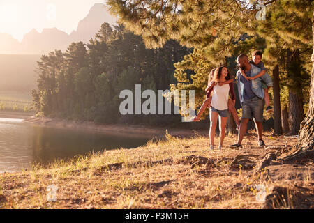 Eltern geben Kindern Piggyback Rides auf Spaziergang am See Stockfoto
