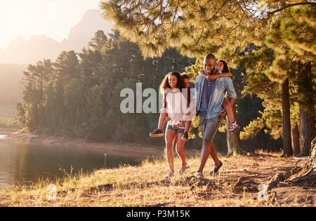 Eltern geben Kindern Piggyback Rides auf Spaziergang am See Stockfoto