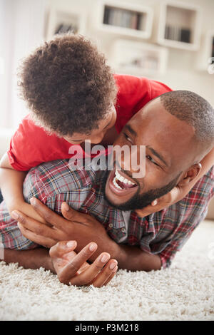 Sohn klettert auf Väter zurück, wie Sie spielen Spiel in der Lounge zusammen Stockfoto