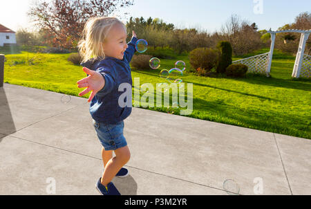 Glückliches weißes Kleinkind, das draußen mit Seifenblasen spielt Stockfoto