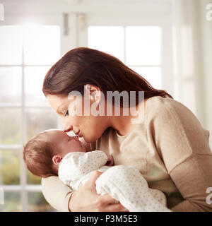Liebevolle Mutter küssen und Kuscheln neugeborenes Baby zu Hause Stockfoto