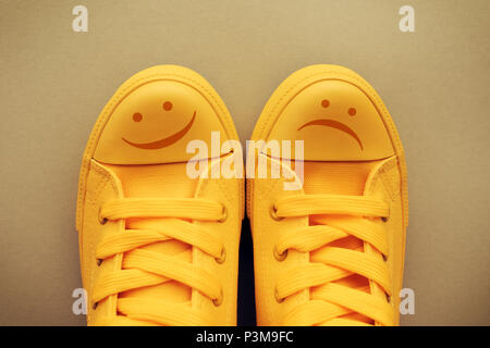 Glückliche und traurige Smiley Emoticon Symbol auf gelbem Sneakers, konzeptionelle Bild für Gefühle und Emotionen der jungen Menschen und Jugendlichen Stimmungsschwankungen Stockfoto