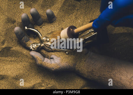 Forensische Experten entdecken Leiche in der Wüste Sand mit Gerechtigkeit Statue in der Hand begraben. Konzeptionelle Bild für die polizeiliche Untersuchung eines kalten Fall mur Stockfoto