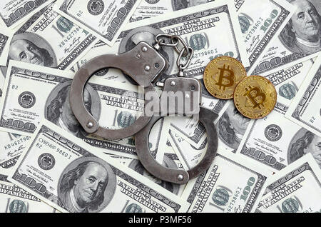 Polizei Handschellen und Bitcoins liegen auf eine große Anzahl von Dollarnoten. Das Konzept der Probleme mit dem Gesetz während der Illegalen cryptocurrency Bergbau- und Stockfoto