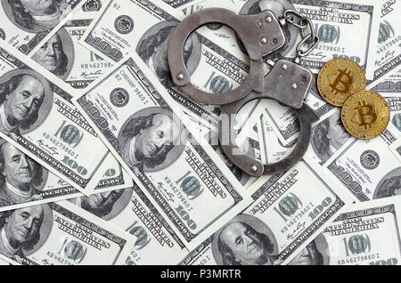 Polizei Handschellen und Bitcoins liegen auf eine große Anzahl von Dollarnoten. Das Konzept der Probleme mit dem Gesetz während der Illegalen cryptocurrency Bergbau- und Stockfoto