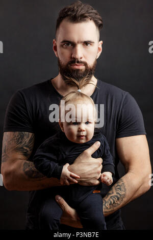 Schön tätowiert gelagert Mann mit niedlichen kleinen Baby auf schwarzem Hintergrund Stockfoto