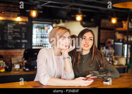 Zwei attraktive junge Freundinnen plaudern auf dem Smartphone im Cafe Stockfoto