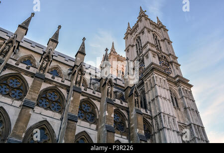 Gotische Westminster Abbey, seitliche Perspektive von unten. Strebebögen, er Fenster im Kirchenschiff und eine der grauen Stein Türmen gegen den blauen Himmel. Stockfoto