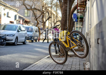 Peking, China - MÄRZ 10, 2016: Fahrräder, Roller und Autos in Peking Straßen. Ein gelbes Fahrrad ist, um den Baum mit der eisernen Kette verbunden. Stockfoto