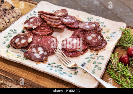 Italienischen Aromen: geschnittene Salami in eine Platte auf einem Holztisch mit Oregano und Kirschen verziert - selektive Fokus Stockfoto