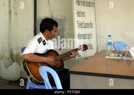 Cham Yeam; am Grenzübergang Check Point zwischen Kambodscha und Thailand eine entspannte Quarantäne Offizier spielt eine abgenutzte Gitarre. Stockfoto