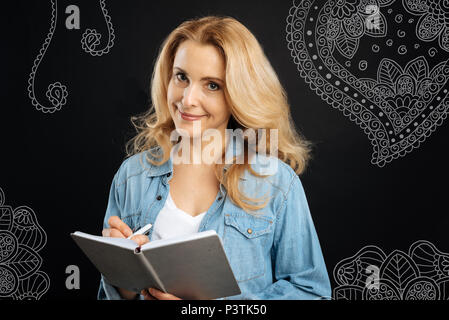 Junge Frau legere Notizen und lächelnd, während Sie ein Notebook Stockfoto