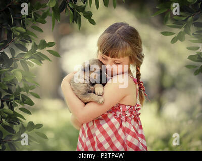 Kleines Mädchen mit kleinen niedlichen Mädchen mit geschlossenen Augen sanft umarmt ein wenig puppya Welpen Stockfoto