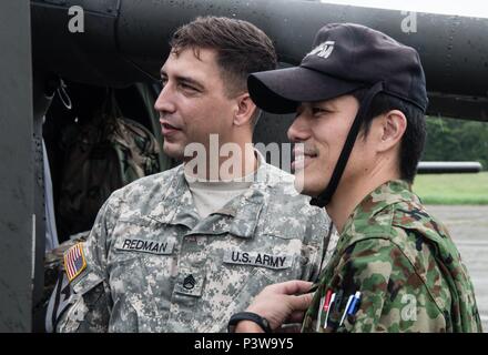 Army Staff Sgt. Joel Redman (links), Crew Chief, U.S. Army Aviation Battalion-Japan, gibt eine Tour durch eine der UH-60 Blackhawk Hubschrauber seiner Maßeinheit zu seinem Japan Masse Verteidigung-kraft Gegenstück während des zweiten Tachikawa Hubschrauber Konferenz durchgeführt, 26. Juli 2016, im Camp Tachikawa, Japan. Durch die JGSDF Östlichen Armee wird die Konferenz trafen sich Vertreter von der japanischen Selbstverteidigungsstreitkräfte, United States Military Zweige, und Japans Zivilluftfahrtbehörden, um Informationen auszutauschen und Strategien Hubschrauber Betrieb während einer Katastrophe zu führen. Wie die auf Stockfoto