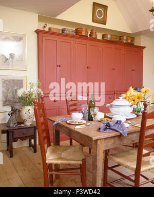 Rush sitzen Stühle an alte Kiefer Tisch für das Mittagessen im Speisesaal mit großen, rosa Einbauschrank eingestellt Stockfoto