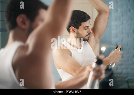 Mann mit Spray deodorant auf Unterarm für schlechten Geruch Stockfoto