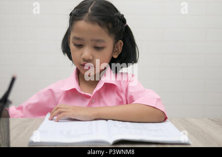 Das kleine Mädchen mit Hausaufgaben. Kinder auf der Suche nach einem Notebook auf dem Holztisch. Wählen Sie Fokus flache Tiefenschärfe. Stockfoto