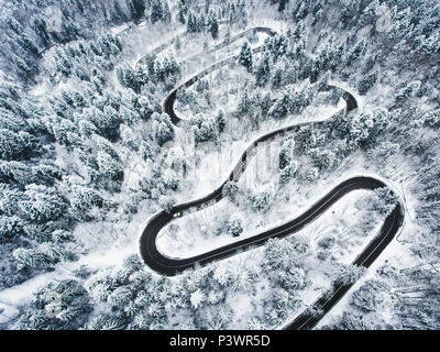Verschneite Straße in den Wald. Extreme kurvenreiche Straße hoch oben in den Bergen Stockfoto