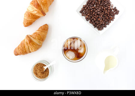 Flach mit kaltem Kaffee brühen, Croissants, brauner Zucker, Milch und Kaffee Bohnen auf weißem Hintergrund. Stockfoto