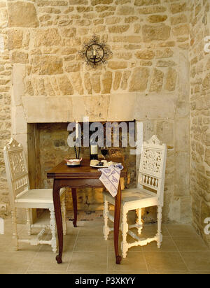 Bemalte Stühle und Tisch für zwei vor dem Kamin im französischen Landhausstil Speisesaal mit Steinwänden Stockfoto