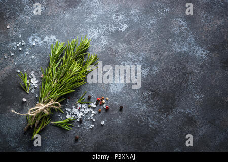 Zweige Rosmarin, Pfeffer und Meersalz auf einem dunklen Stein Hintergrund. Zutaten zum Kochen, Ansicht von Oben, Kopieren. Stockfoto