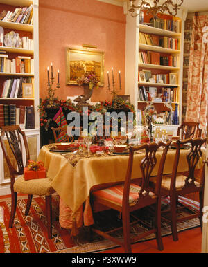 Bücherregale entweder Seite der Kamin mit festlichem Laub Garland und brennende Kerzen in Esszimmer mit Tisch für Weihnachten Abendessen Stockfoto