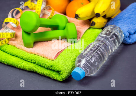 Auf grauem Hintergrund Sportgeräte, Wasser, Hanteln und Obst Stockfoto