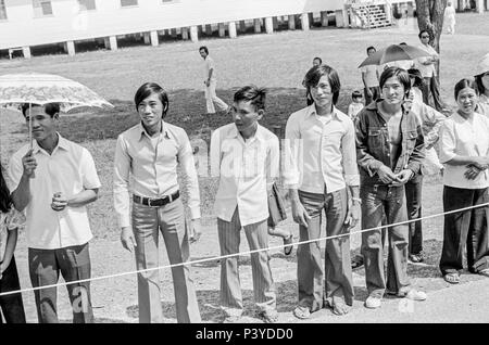 FORT SMITH, AR, USA - 10. August 1975 - Junge vietnamesische Männer und andere Flüchtlinge an der Straße stehen, dass Präsident Gerald Ford's Limo wird, da er kommt das Fort Chaffee vietnamesischen Flüchtlingslager zu bereisen. Stockfoto