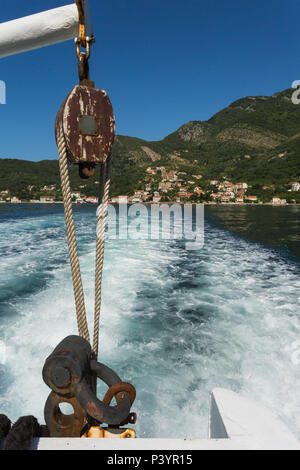 Blick auf Kamenari und Seil Riemenscheibe aus Stahl Arm auf der Rückseite des Kamenari-Lepetane Fähre ausgesetzt ist, Bucht von Kotor, Montenegro mit Wasser aufwachen Trail hinter sich Stockfoto