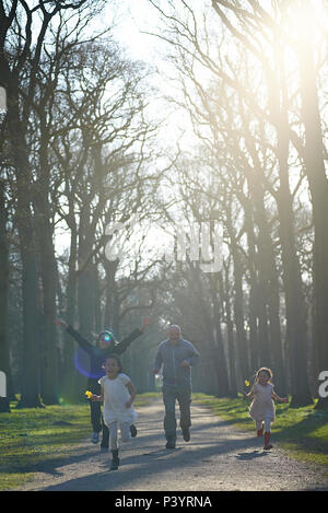 Eine Familie von vier, zwei Eltern und zwei Kindern glücklich zusammen, die in einem Park im Frühling Sonnenschein Stockfoto