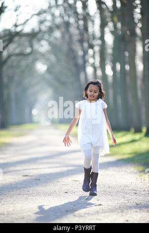 Süße asiatische Mädchen in einem weißen Kleid zu Fuß auf einen Weg in die Perspektive in einem Park in der schönen Frühlingssonne Stockfoto