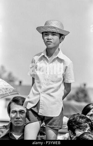 FORT SMITH, AR, USA - August 10, 1975 -- ein kleiner Junge steht vor einer Masse der neu angekommenen Vietnamesische Flüchtlinge auf die wagenkolonne von Präsident Gerald Ford als der Präsident kommt zu begrüßen Flüchtling Fort Chaffee, AR. Stockfoto