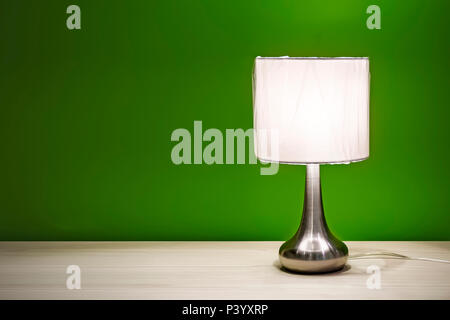 Nachttischlampe auf dem Tisch für den Innenbereich isoliert. Nacht Lampe mit runden Schatten stehend auf einem Holztisch, auf dem Hintergrund der grüne Wände bur zu lesen Stockfoto