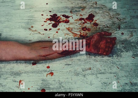 Hand in Blut auf einem weißen Vintage schmutzigen Fußboden in einer Blutlache. Schneiden Sie die Adern auf der Hand eines Selbstmord. Mord mit einem Messer. Stockfoto