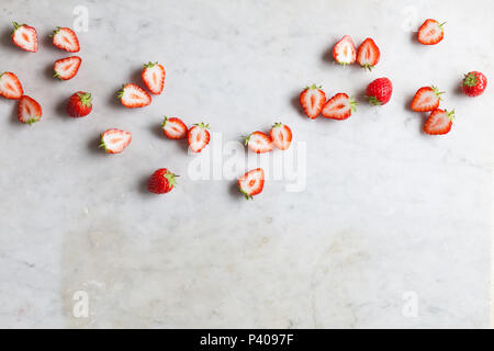 Mischung aus ganze und halbierte Erdbeeren verstreut auf weißem Marmor Arbeitsplatte Stockfoto