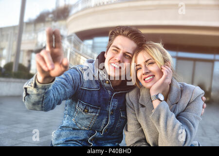 Attraktive junge Paare sitzen auf dem Boden in Urban Street und Träumen über etwas. Stockfoto