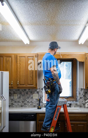 Kaukasische mann Elektriker stehen auf Leiter und ändern Sie leuchtet während einer Küche Renovieren in Wichita, Kansas, USA. Stockfoto