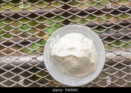 Schlagsahne in die weiße Schale auf dem Metall Tisch gegen Sonnenlicht Hintergrund. Stockfoto