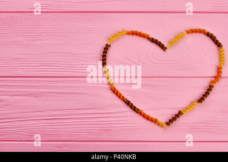 Herz aus getrockneten Teigwaren und Kopieren. Herz Rahmen aus Fusilli auf rosa Holz- Hintergrund. Happy Valentines Tag. Stockfoto